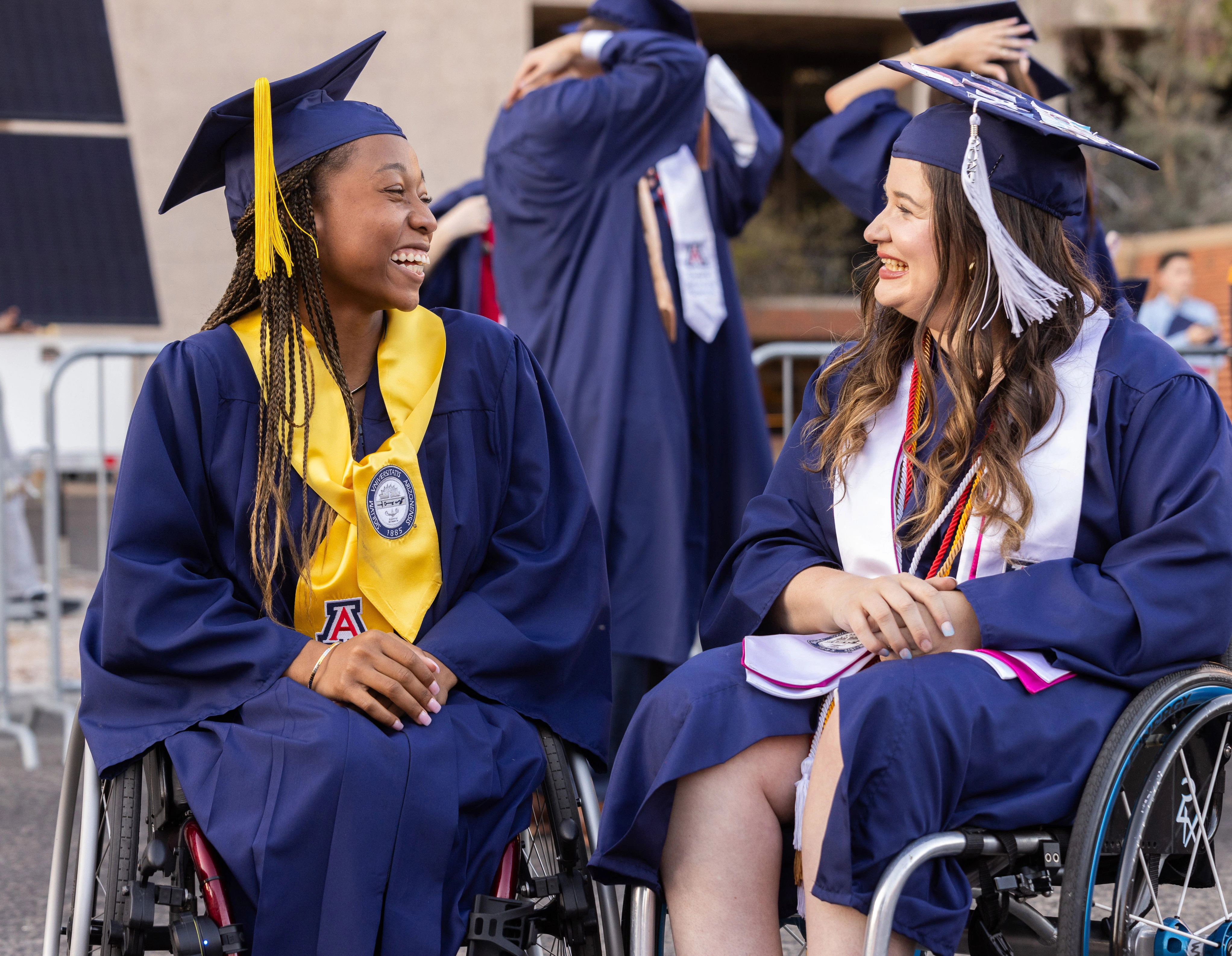 two students in graduation cap and gown smiling at eachother